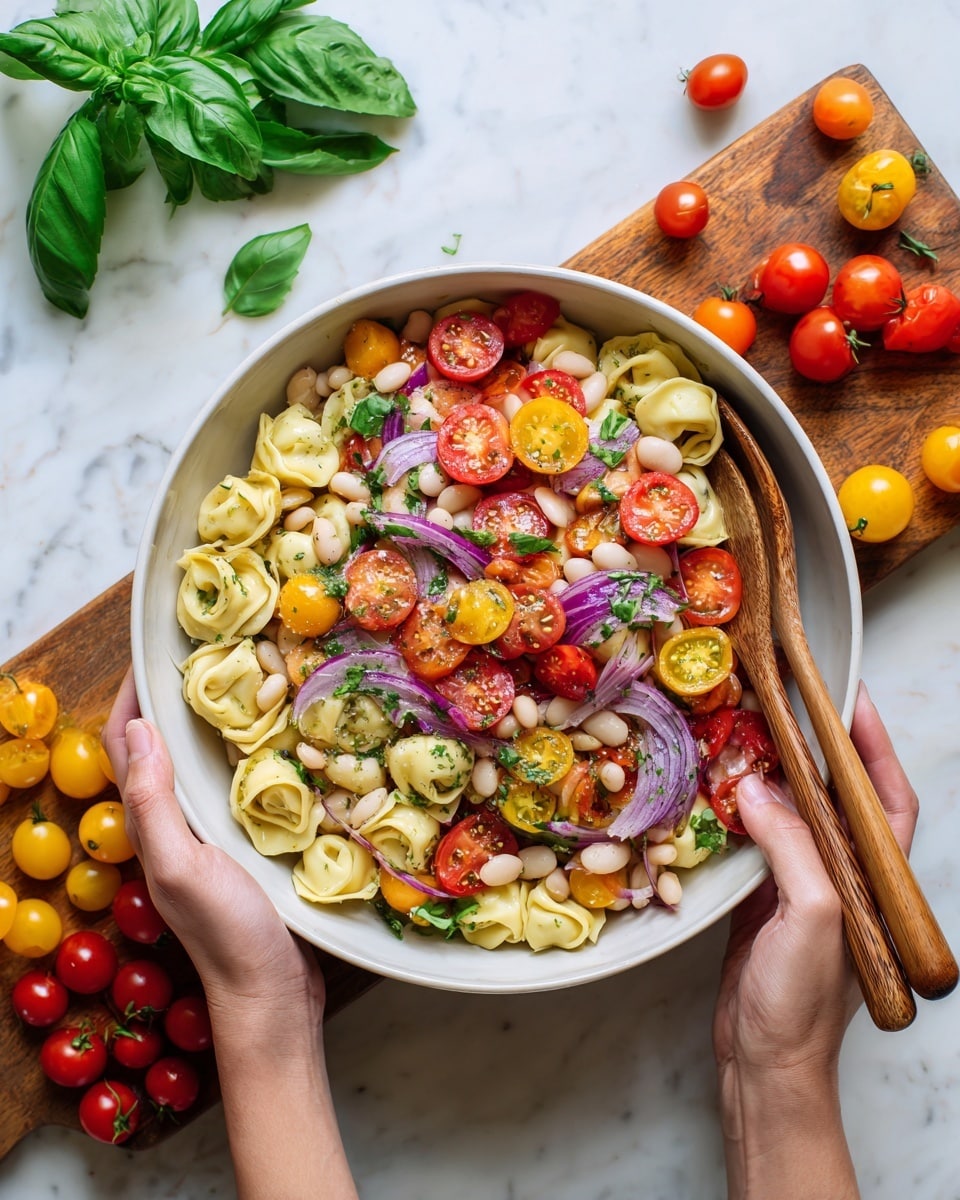 A white bowl filled with a colorful pasta salad with three main layers: the bottom layer of light yellow tortellini pasta, the middle layer of white beans, and the top layer of halved bright red and yellow cherry tomatoes mixed with thin slices of purple onion. The salad is mixed with herbs giving small green details. Woman's hands are holding two wooden spoons to toss the salad. The bowl sits on a white marbled surface with fresh green basil leaves to the top left and clusters of red and yellow cherry tomatoes arranged around the bowl and on a wooden board nearby. photo taken with an iphone --ar 4:5 --v 7