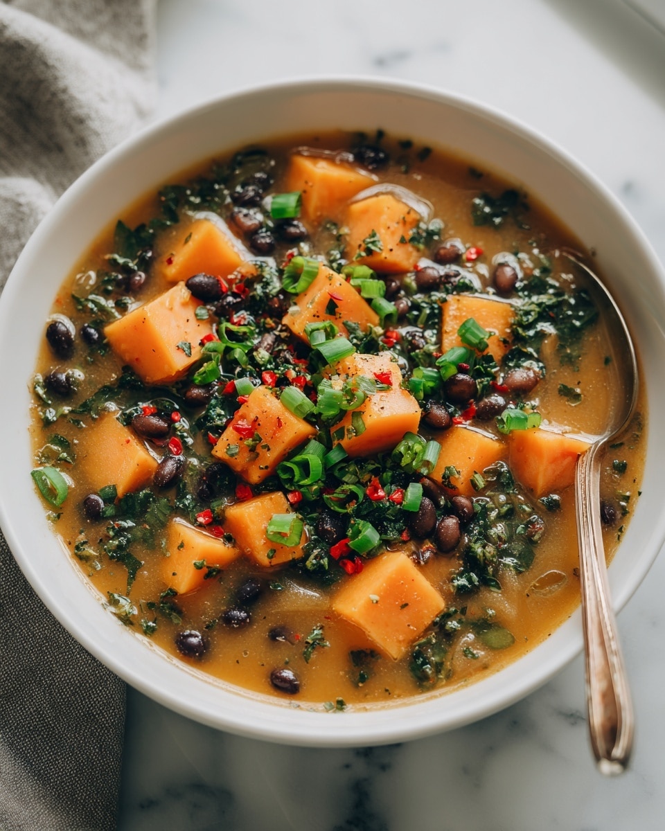 A white bowl filled with a thick soup shows three main layers: large bright orange chunks of sweet potato, many small black beans, and a red-orange broth as the base. On top, fresh green cilantro leaves, chopped green onions, and small pieces of red bell pepper add color and texture. The bowl sits on a white marbled surface near a window with soft natural light highlighting the warm colors of the soup photo taken with an iphone --ar 4:5 --v 7