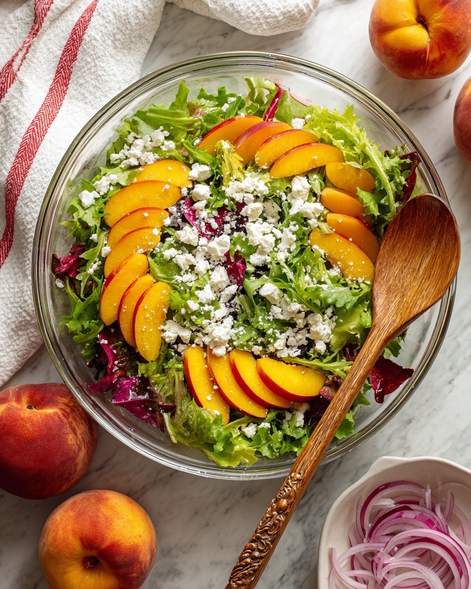 A large clear glass bowl holds a fresh mixed green salad with several layers; the bottom layer is leafy greens of different shades of green and purple, the middle layer has bright orange peach slices evenly spread, and the top layer is sprinkled with white crumbled cheese, giving a textured look. A wooden spoon with a detailed handle rests on the right side inside the bowl. The bowl sits on a white marbled surface, near two whole peaches on the bottom left and a small white dish with sliced red onions in the top right corner. Part of a white cloth with red stripes is visible in the top left corner of the scene. Photo taken with an iphone --ar 4:5 --v 7