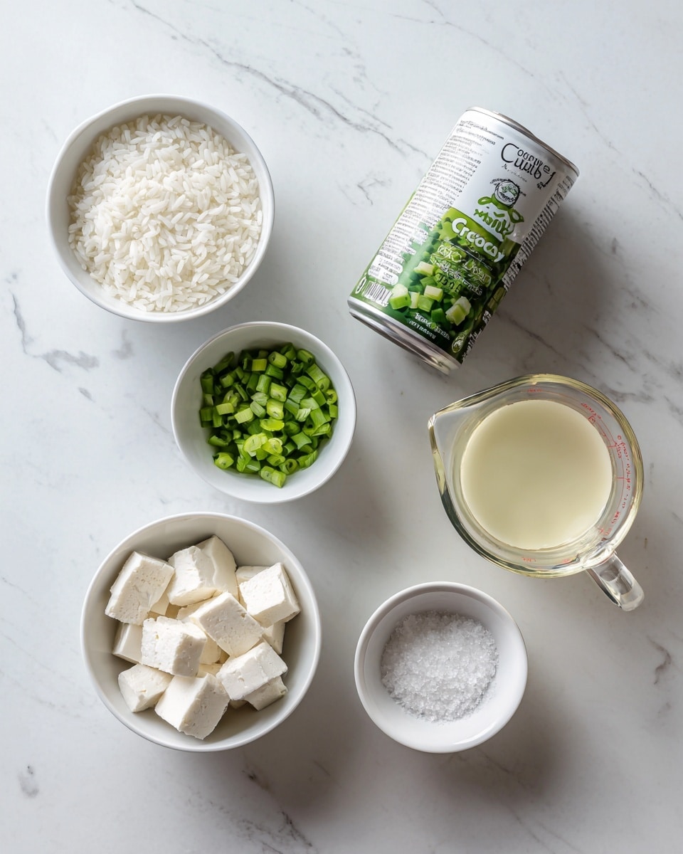 The image shows six white bowls and a glass measuring cup arranged neatly on a white marbled surface. Starting from the top left, there is a white bowl filled with white rice grains. Below it, a smaller white bowl contains chopped green onions. Near the center, a can of coconut milk sits upright with its label facing forward, displaying green and white colors. To the right of the can, a clear glass measuring cup holds a pale yellow liquid. Below the measuring cup, a small white bowl holds a white granular ingredient, possibly salt. At the bottom left, a white bowl contains several small white cubes, likely tofu. The overall arrangement is neat and clear, showcasing each ingredient separately with natural lighting. Photo taken with an iphone --ar 4:5 --v 7