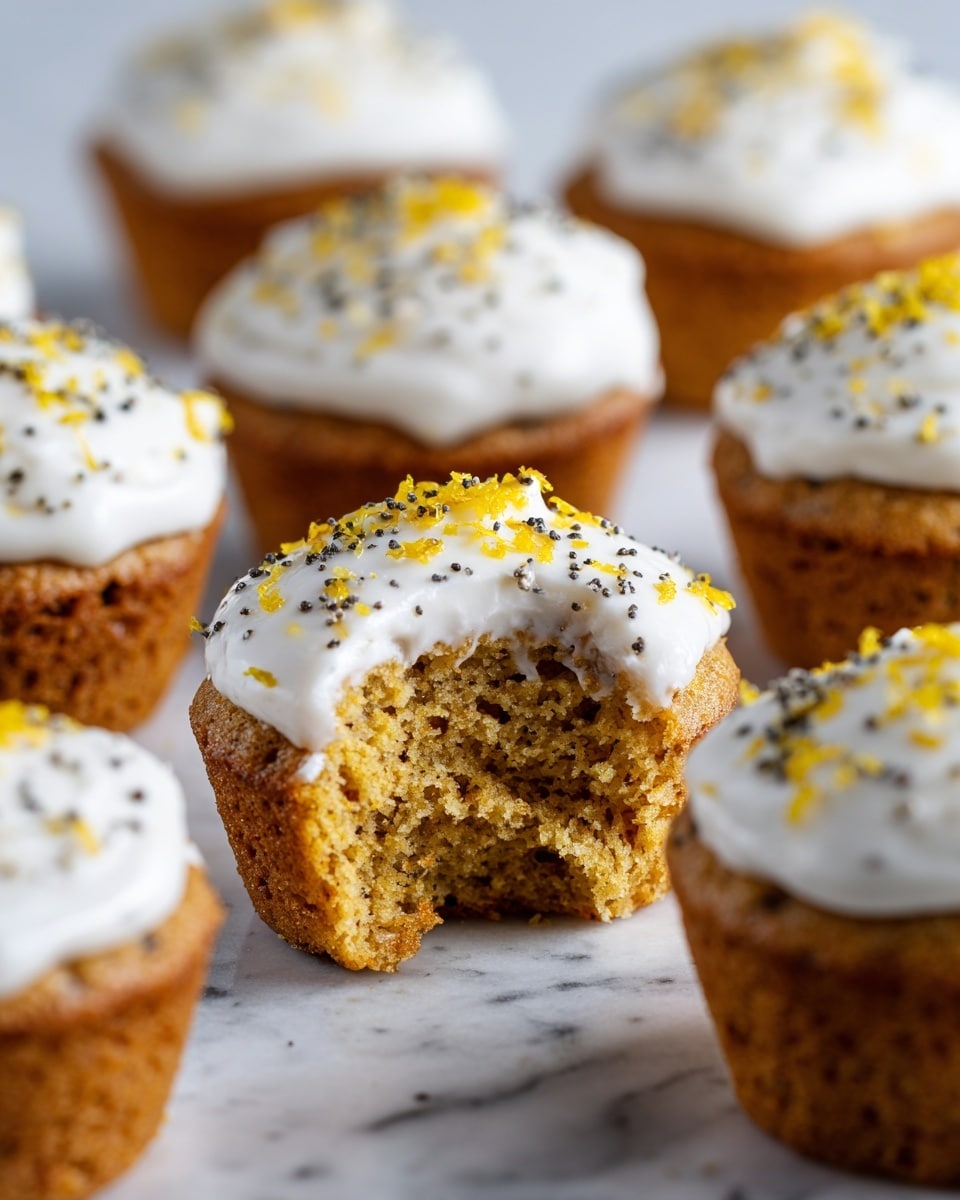The image shows multiple small golden brown muffins arranged on a white marbled surface. Each muffin has a thick layer of white frosting on top sprinkled with tiny black seeds and bright yellow zest. The muffin in the front is missing a bite, showing its soft and moist inside with a light crumb texture. The muffins have a slightly rough surface and a warm baked color. Photo taken with an iphone --ar 4:5 --v 7