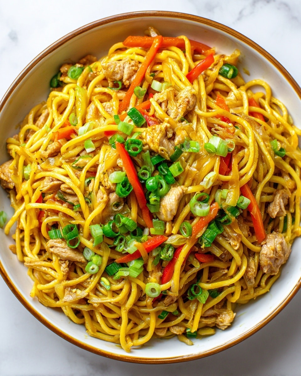 A close-up top view of a bowl filled with thick yellow noodles mixed with small brown pieces of cooked chicken. The noodles and chicken are spread evenly and mixed with thin slices of orange bell pepper and cooked onions, creating a vibrant and colorful layer. On top, bright green chopped fresh scallions are sprinkled, adding a fresh touch. The bowl is white with a light brown rim, sitting on a white marbled surface. photo taken with an iphone --ar 4:5 --v 7