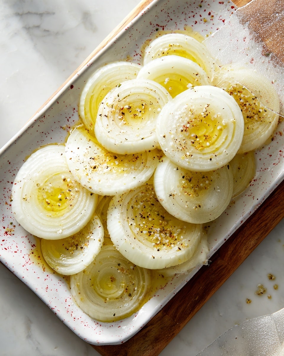 A white tray with red splatter pattern holds around thirteen round white onion slices stacked in layers, each slice with a center pool of yellow oil and sprinkled with coarse salt crystals. The tray sits on a white marbled surface next to a clear plastic bag and a wooden cutting board. Sunlight shines on the top right corner of the tray, highlighting the glossy texture of the oil on the onions. The onion slices are smooth and shiny with slightly translucent layers, arranged casually in the tray. photo taken with an iphone --ar 4:5 --v 7