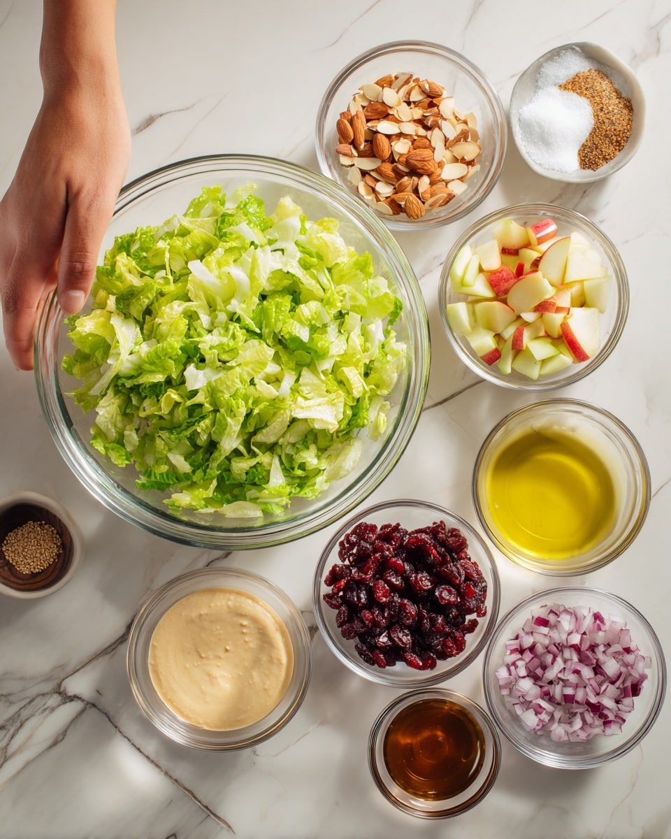 The image shows several clear glass bowls arranged on a white marbled surface. The largest bowl contains bright green chopped lettuce with some white parts. Four medium bowls surround it: one with light tan almond slices, one with red chopped apples, one with reddish dried cranberries, and one with finely chopped purple onions. Five small bowls hold different dressings and spices: a smooth light beige cream, a thick golden honey-like liquid, a clear yellow oil, a dark brown sauce, and a small amount of brown seeds and salt. A woman’s hand is reaching from the left side toward the bowls. photo taken with an iphone --ar 4:5 --v 7