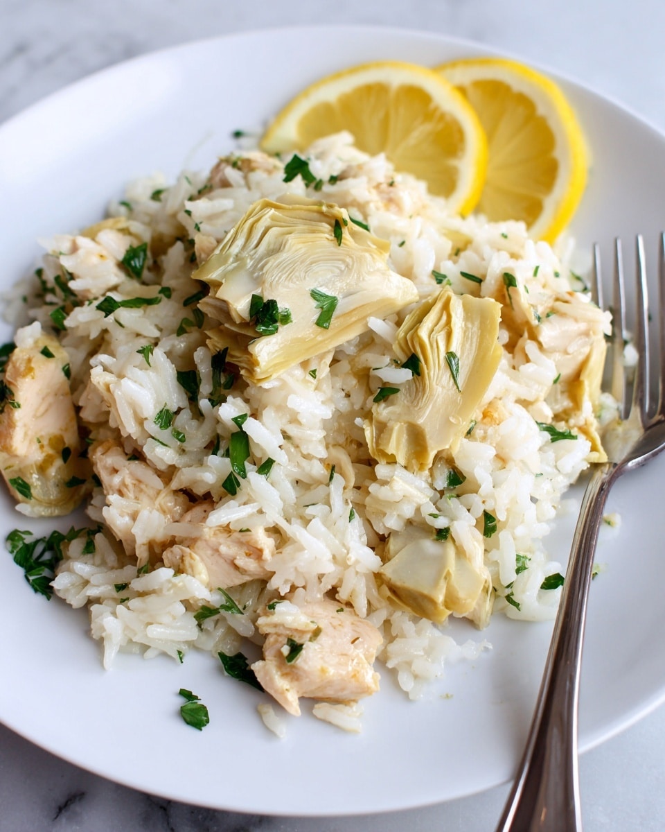 A close-up of a white plate with a light ridged pattern shows a mixed dish of light yellow and white rice layers scattered with small pieces of cooked light beige chicken and tender artichoke pieces. The dish is topped with bright green chopped herbs and garnished with two thin yellow lemon slices placed at the upper edge of the plate, partially visible behind the rice. A metal fork is positioned near the rim on the right side, closely touching the food. The plate rests on a white marbled surface photo taken with an iphone --ar 4:5 --v 7
