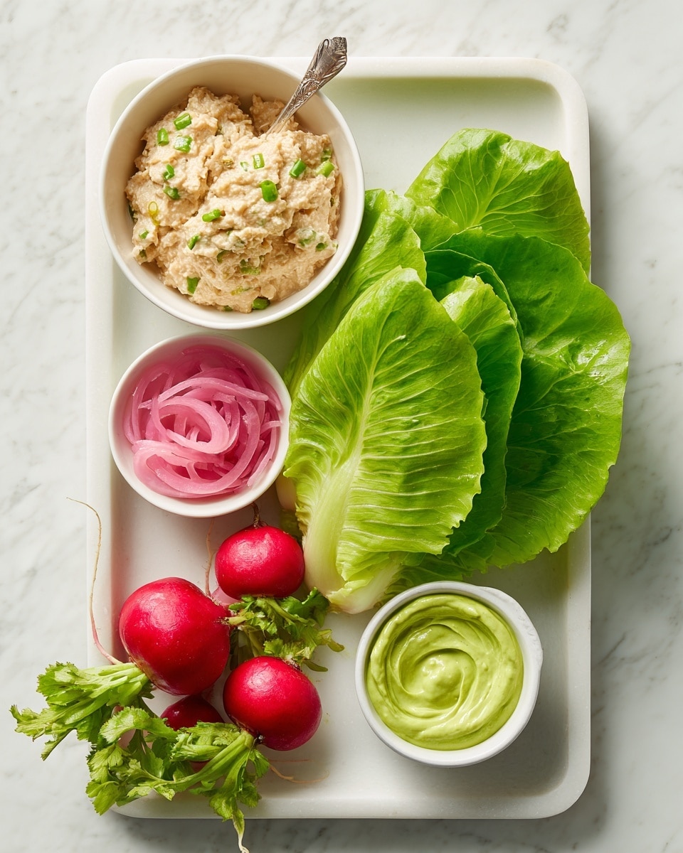 The image shows a white tray on a white marbled surface holding several fresh ingredients. At the top left, a small white bowl contains a chunky, light beige mixture with small green bits and a spoon. To the right of this bowl are large, bright green butter lettuce leaves stacked loosely. Below the lettuce, on the right side, there is a small white cup with a green creamy sauce swirled smoothly inside. At the bottom left corner of the tray, fresh radishes with bright red skins and green leafy tops are arranged in a small bunch. Between the radishes and lettuce, a small white bowl holds thin, bright pink pickled onion rings. The overall setting is clean and fresh with a focus on green and red colors. photo taken with an iphone --ar 4:5 --v 7