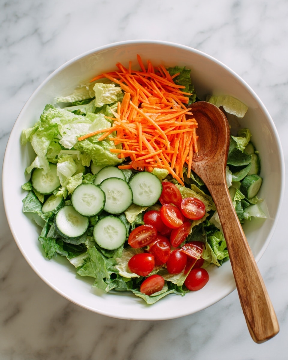 A white bowl filled with fresh salad layers sits on a white marbled surface. The bottom layer consists of light green leafy lettuce with a soft, crinkled texture, covering the base. On top, bright orange shredded carrots are sprinkled unevenly, adding a thin, stringy texture. Scattered throughout are vibrant red cherry tomatoes with smooth skin, and slices of cucumber showing pale green centers with darker green edges, giving a fresh look. A wooden spoon is placed inside the bowl, partially resting on the salad. The overall presentation is fresh and colorful, photo taken with an iphone --ar 4:5 --v 7