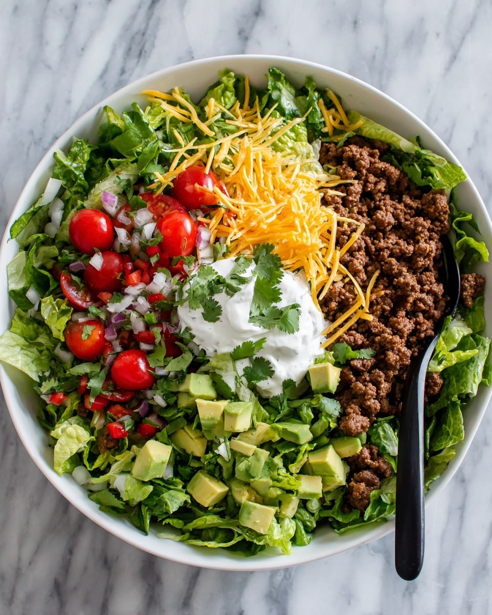A large white bowl sits on a white marbled surface filled with a colorful layered salad. The bottom layer is bright green torn leafy lettuce, topped with crumbly browned ground meat scattered unevenly. Next are small wedges of yellow cheese and sliced cherry tomatoes halved to show their juicy interior. Over the middle sits a dollop of white sour cream garnished with a small cilantro leaf. Around it, chopped avocado pieces in pale green and fresh tomato salsa with red tomato chunks mixed with onion and herbs are spread. The salad is finished with loose shredded cheese and fresh cilantro leaves sprinkled all over. A black fork is stuck into the bowl. Photo taken with an iphone --ar 4:5 --v 7