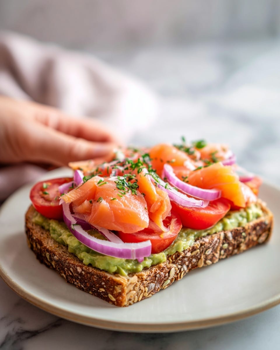 Two slices of seeded brown bread are placed on a white plate set on a white marbled surface. Each slice has a layer of bright green mashed avocado spread evenly. On top of the avocado is a generous layer of white creamy cheese. Over the cheese, light orange slices of smoked salmon are loosely folded, showing a smooth and soft texture. Thin rings of purple onion and small green capers are scattered on the salmon. The dish is finished with small sprigs of fresh green dill and a light sprinkle of dried herbs. Photo taken with an iphone --ar 4:5 --v 7