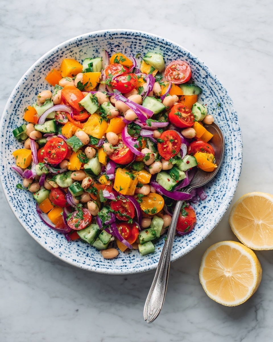 A colorful bean salad sits in a white bowl with blue splatter details, filled with layers of cream-colored beans, bright orange bell pepper pieces, green cucumber chunks, and halved red cherry tomatoes. Thin rings of light purple onion and small bits of green herbs are mixed throughout, giving texture and freshness. A silver spoon rests on the right side of the bowl. The bowl is placed on a white marbled surface with two squeezed lemon halves nearby. Photo taken with an iphone --ar 4:5 --v 7