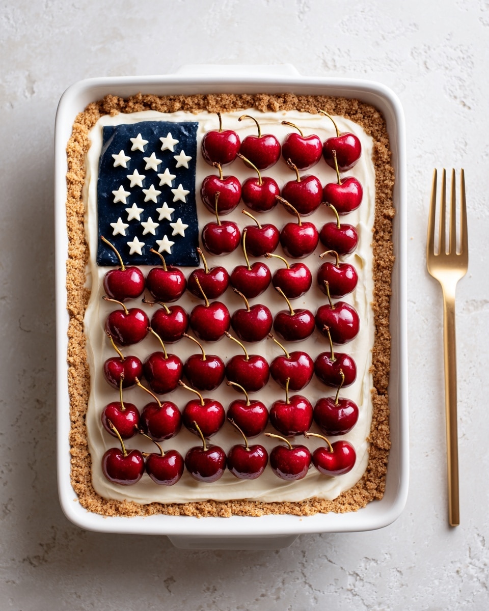 The dish is a rectangular dessert topped to look like an American flag. There are seven bright red strips made from cherry halves running horizontally across a smooth white cream layer, which represents the stripes. In the top left corner, there is a square section filled with small white star shapes scattered over a dark purple-blue berry topping. The dessert sits in a white rectangular dish on a white marbled surface, with a gold fork placed to the side. Photo taken with an iphone --ar 4:5 --v 7