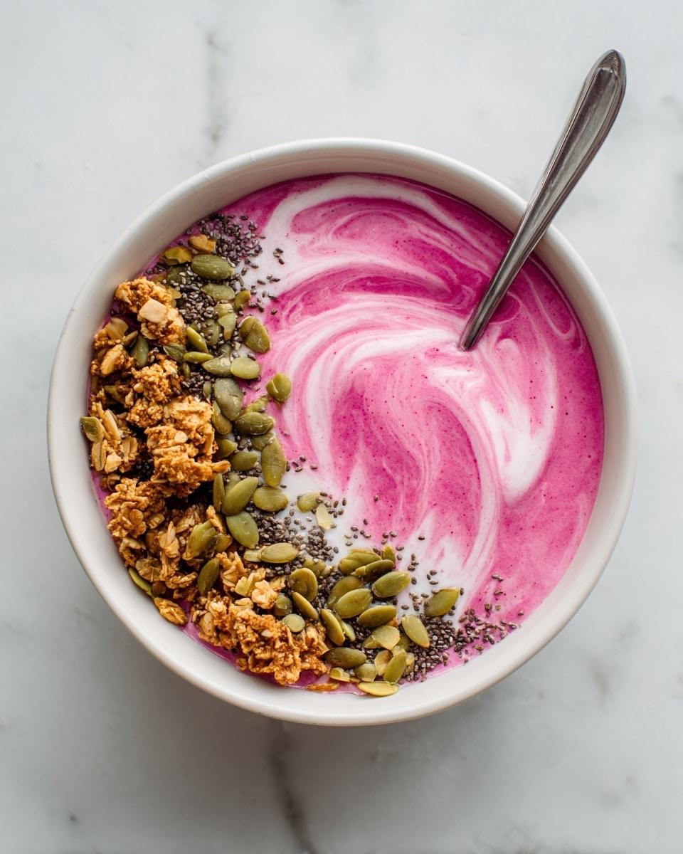 A white bowl filled with a vibrant bright pink creamy smoothie base, swirled with smooth texture and topped with three main layers: crunchy granola with light brown clusters, whole almonds, and green pumpkin seeds on one side, with white coconut flakes scattered around the center. The bowl sits on a white marbled surface, and there is a silver spoon inside the bowl on the left side. photo taken with an iphone --ar 4:5 --v 7