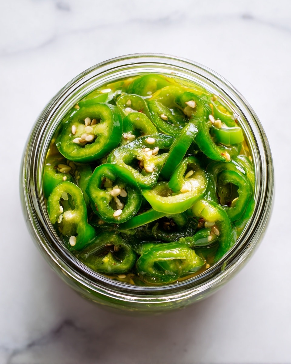 A clear glass jar filled with many slices of green pickled peppers, each slice showing a shiny, wet texture with visible seeds inside, bright green colors ranging from light to dark, tightly packed to fill the jar all the way to the top, placed on a white marbled surface, photo taken with an iphone --ar 4:5 --v 7