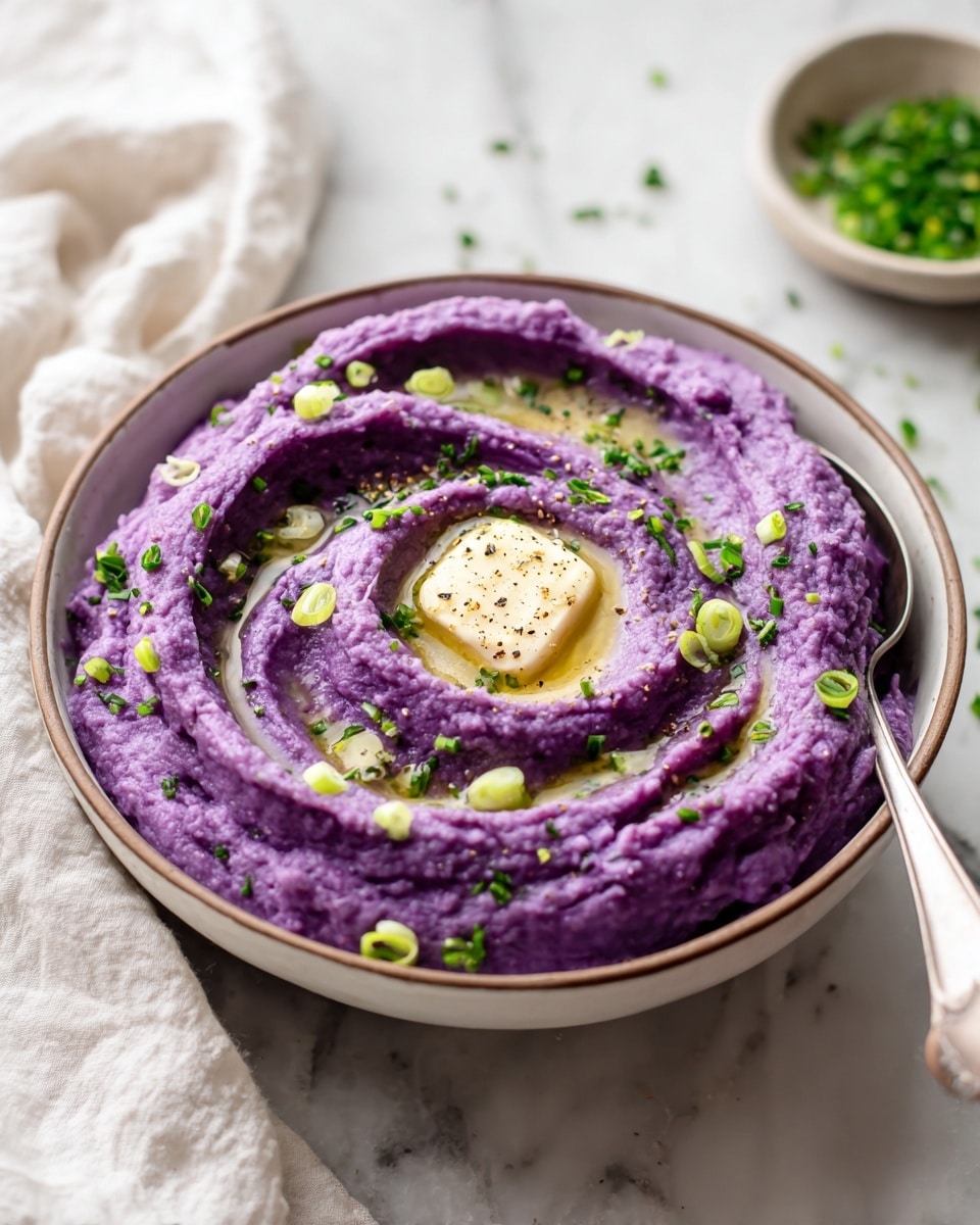 The image shows a white bowl filled with bright purple mashed potatoes, with a small melting dollop of butter in the center creating a glossy spot. The texture of the mash is smooth with some rough swirls and ridges all around. There are green onion pieces and chopped parsley sprinkled over the top, adding green color contrasts. A silver spoon rests inside the bowl on the right edge. The bowl sits on a white marbled surface, with a white cloth nearby and some scattered green herbs around. photo taken with an iphone --ar 4:5 --v 7
