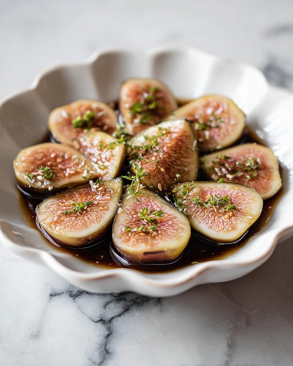 A white scalloped ceramic dish holds halved figs arranged in a single layer, showing their light brown and pinkish interiors with a soft texture. The figs sit in a dark brown liquid which spreads evenly across the bottom of the dish. Small green herb pieces are sprinkled on top, adding a fresh color contrast. The dish is placed on a white marbled surface. Photo taken with an iphone --ar 4:5 --v 7