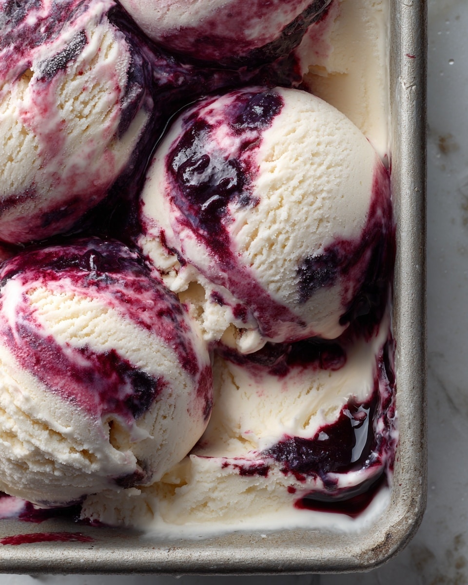A close-up scoop of creamy ice cream with visible swirls of dark purple berry sauce mixed throughout, placed inside a metal pan that shows texture and cold moisture droplets on its surface, all set on a white marbled background. The ice cream has a smooth texture with a slightly uneven surface where the berry sauce blends into the creamy base. Photo taken with an iphone --ar 4:5 --v 7