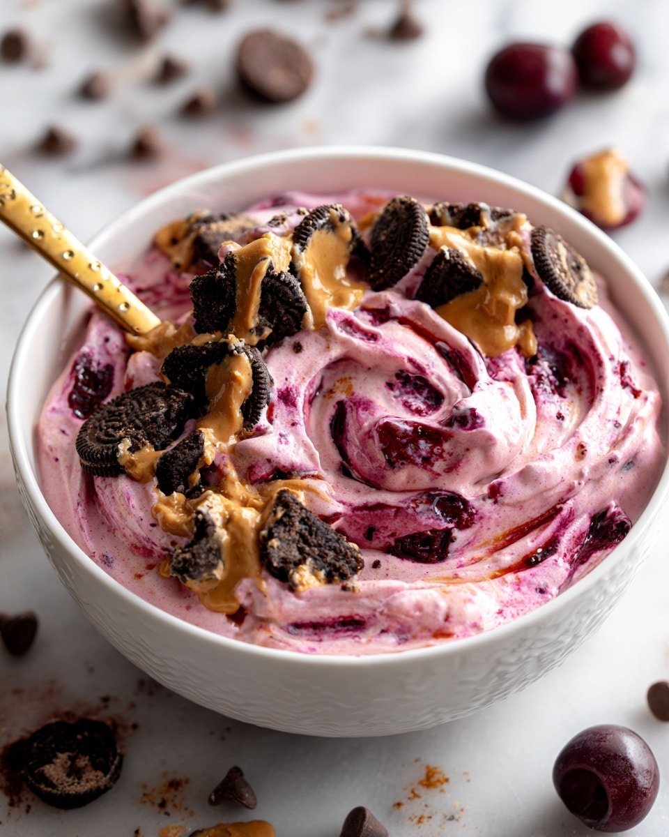 A white bowl filled with creamy pink yogurt mixed with dark red cherry pieces and small dark chocolate chips. On top, there are broken chocolate cereal squares scattered unevenly, drizzled with a light brown nut butter sauce. A long gold spoon stands inside the bowl, and the bowl rests on a white marbled surface with a few fresh cherries around. Photo taken with an iphone --ar 4:5 --v 7