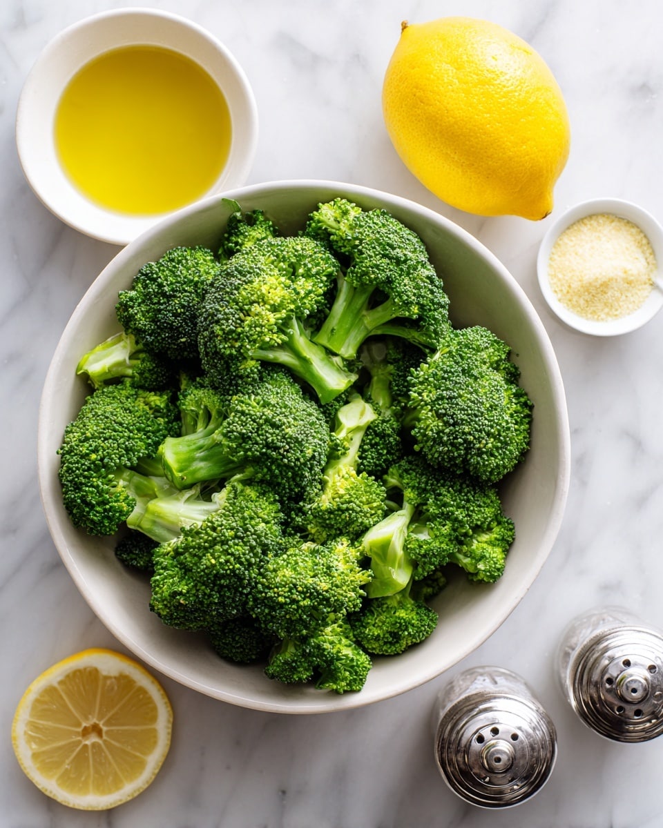 A white bowl filled with fresh green broccoli florets sits on a white marbled surface. Next to the bowl, there is a whole bright yellow lemon and a small white bowl with golden olive oil. Nearby, there is a small white bowl containing a light yellow powder, likely cheese or seasoning, and a silver salt shaker. The overall look is clean and fresh with vibrant green, yellow, and white colors. Photo taken with an iphone --ar 4:5 --v 7