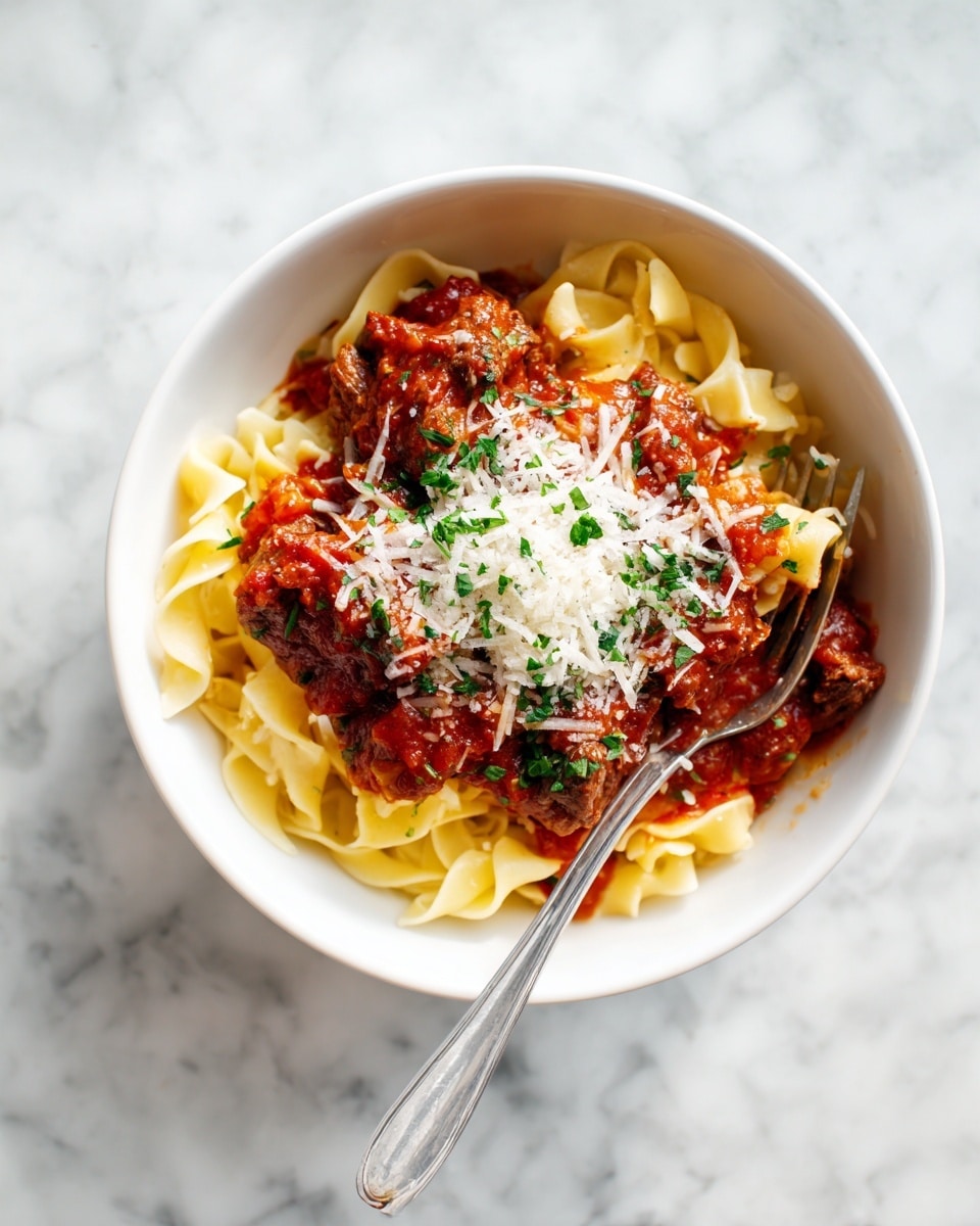A white bowl filled with three layers of food: the bottom layer is a bed of long, flat, yellowish pasta noodles twisted and slightly glossy, coated in a thick red tomato sauce with visible bits of cooked chunks of meat and sauce specks. The middle layer shows more sauce with pieces of meat evenly mixed in. The top layer has a small heap of finely grated light yellow cheese sprinkled with small green herb bits. A fork leans inside the bowl on the right side. The bowl is placed on a white marbled surface. photo taken with an iphone --ar 4:5 --v 7